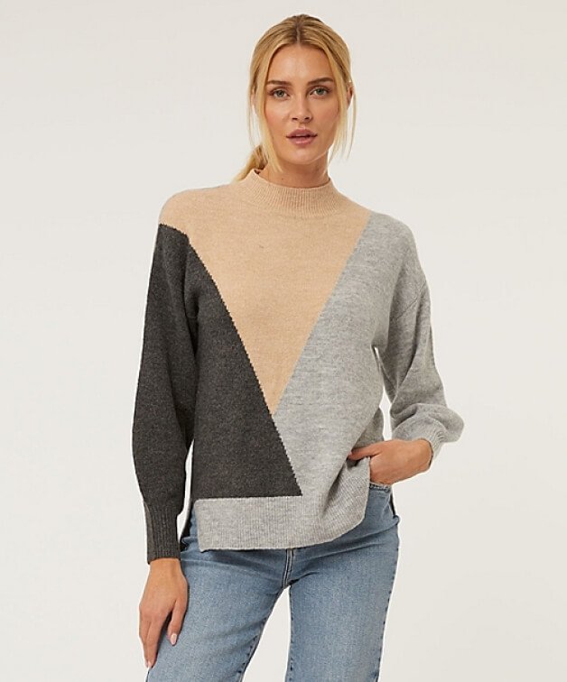 A woman posing in a geometric jumper and jeans